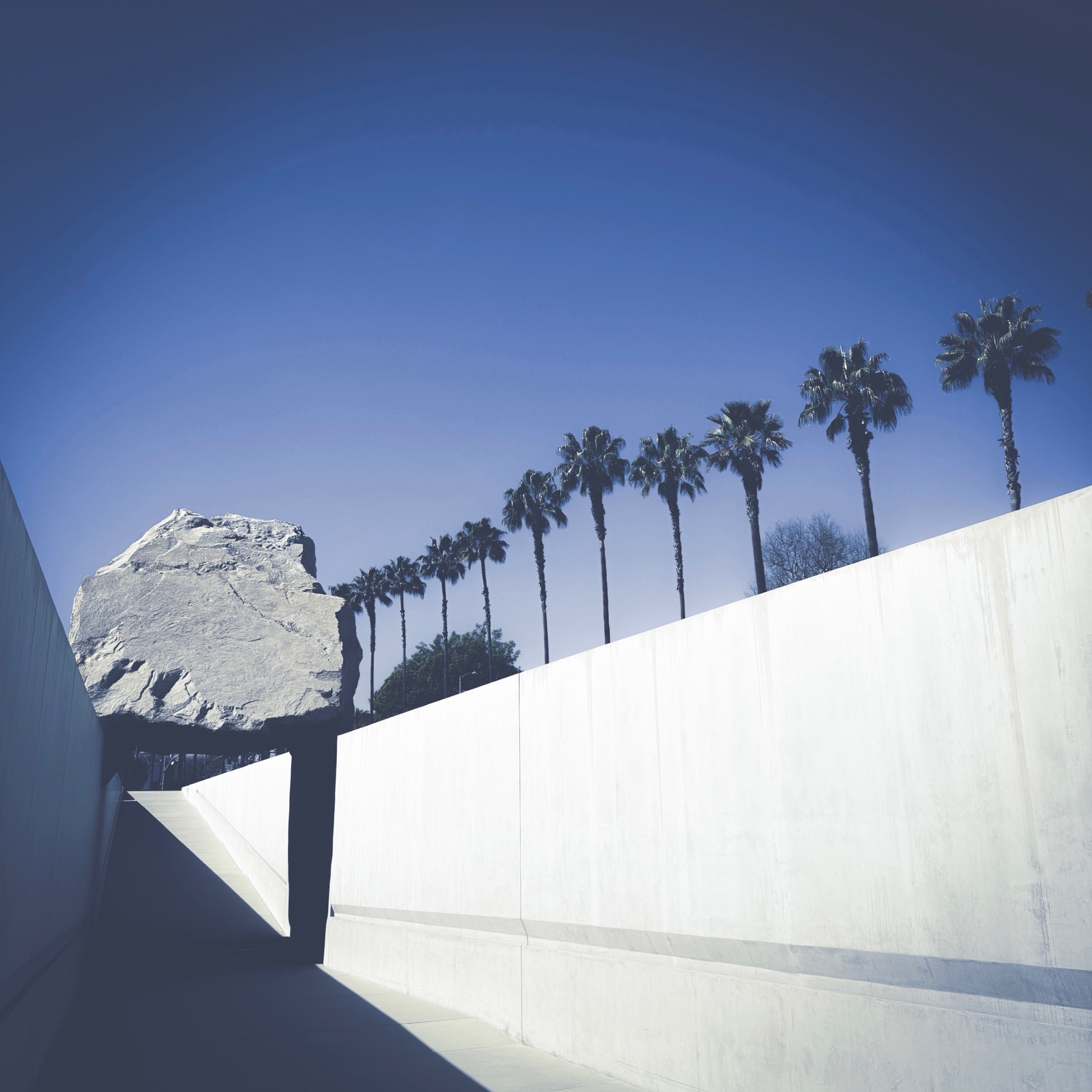 Levitated Mass, Michael Heizer's boulder sculpture at LACMA, seen from the walkway beneath it against a line of palm trees